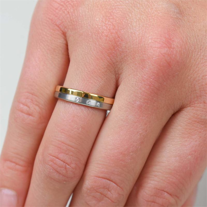 Close-up van een hand met twee ringen: een gouden golvende band en de Boccia Titanium Ring Bicolor dia 3/0.015 - 0129-04 van Boccia, beide gestapeld op de ringvinger.