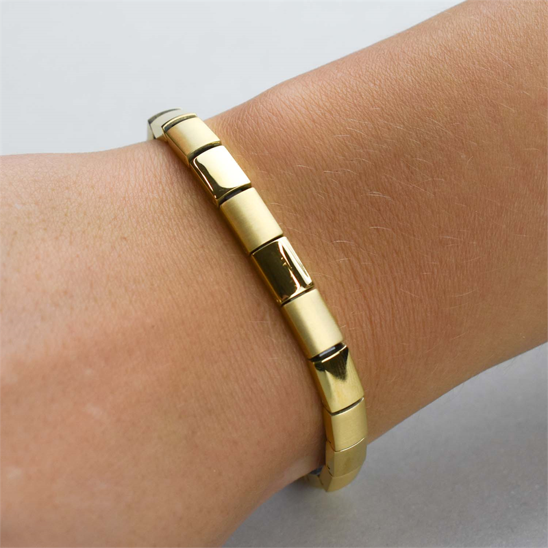 Een close-up van een pols die de Boccia Titanium Armband gp 0313-10 van Boccia draagt, met een slanke, goudkleurige afwerking en een gepolijst, gesegmenteerd ontwerp tegen een effen achtergrond.