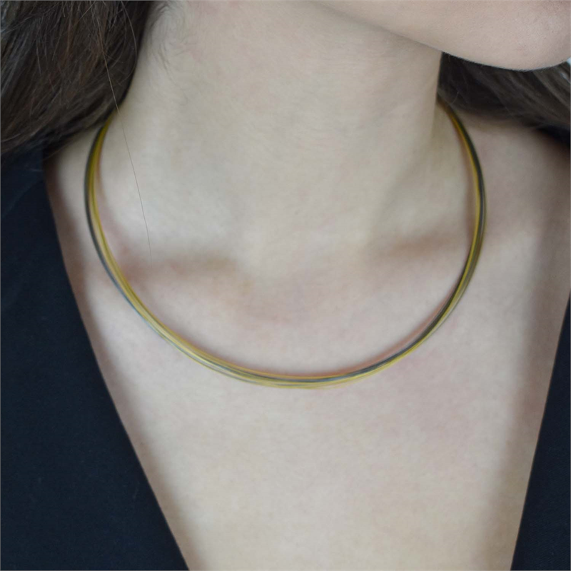 Een close-up toont een persoon die de Boccia Titanium Lengte Collier Bicolor staal 0859-03 draagt, een slanke tweekleurige choker halsketting van Boccia, gecombineerd met een zwart topje en met nadruk op de hals en het sleutelbeen.