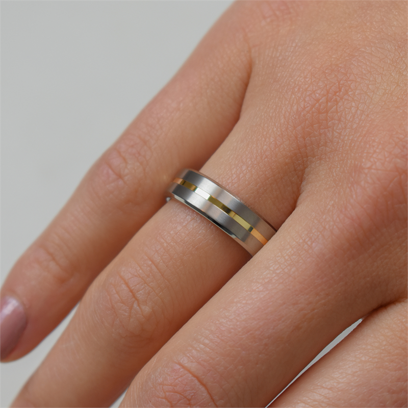 Een close-up van een hand met de Boccia Titanium Ring Bicolor 0101-03 van Boccia, met gouden en zwarte strepen. De korte nagels met lichtroze nagellak accentueren het goudkleurige accent van de ring.
