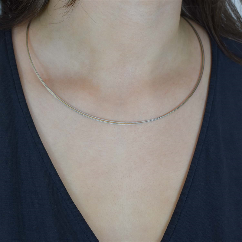 Een close-up toont iemand in een donker topje met V-hals en een Boccia Titanium Lengte Collier Bicolor staal 0804-02, een dunne, zilveren choker met een elegante banjonetsluiting van titanium, waardoor de ingewikkelde details prachtig worden benadrukt.