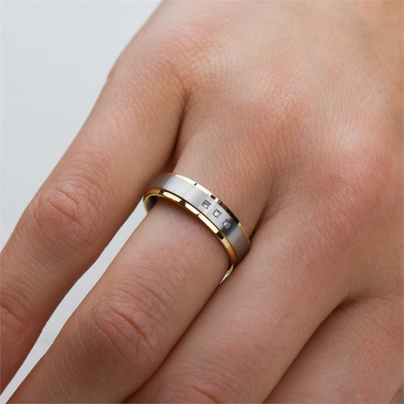 Een close-up van een hand die de Boccia Titanium Ring Bicolor 0134-04 draagt, toont de gouden en zilveren banden. Dit elegante titanium stuk heeft vijf kleine gegraveerde symbolen, rustend op een neutrale achtergrond die het prachtige ontwerp benadrukt.