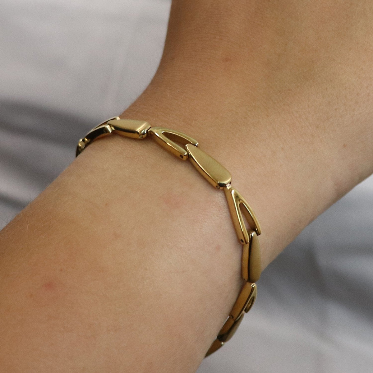 Een close-up van een pols met de Boccia Titanium Armband gp 03033-03 met goudkleurige rechthoekige, licht gebogen schakels. De zachte achtergrond benadrukt dit elegante Boccia sieraad.