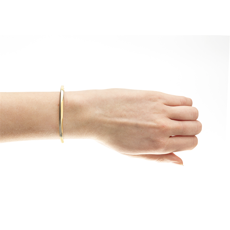 Een hand met een Boccia Titanium Armband Spang Bicolor 03011-02 is afgebeeld tegen een witte achtergrond. De dunne gouden armband rust losjes om de pols, met de vingers licht gebogen in een ontspannen positie.