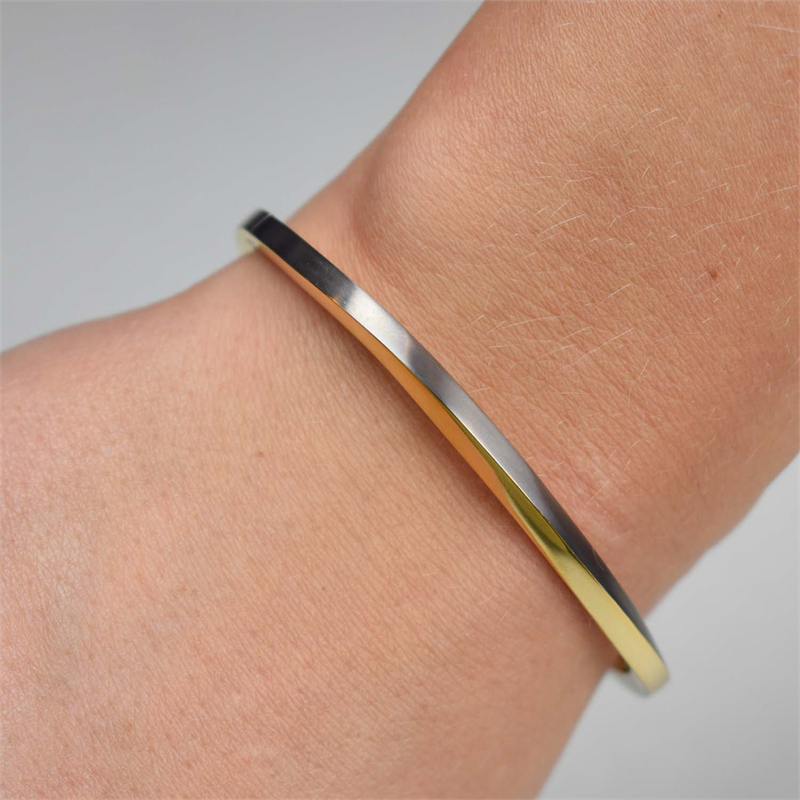 Een close-up van een pols met de strakke Boccia Titanium Armband Spang Bicolor 03011-02 toont een gladde tiara met een elegant goud-zwart verloop tegen een zachte, neutrale achtergrond.