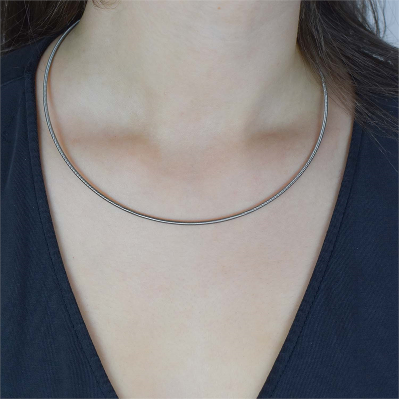 Iemand die de Boccia Titanium Lengte Collier 0808-01 draagt, een slanke en dunne titanium ketting van Boccia, gecombineerd met een diep V-hals zwart topje dat de halslijn en het sleutelbeen benadrukt.