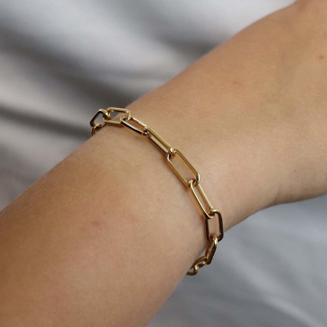 Een close-up van een pols versierd met de Boccia Titanium Armband gp 03045-02 van Boccia, met vergulde titanium paperclipschakels met langwerpige rechthoekige schakels tegen een zachte, lichtgekleurde achtergrond.