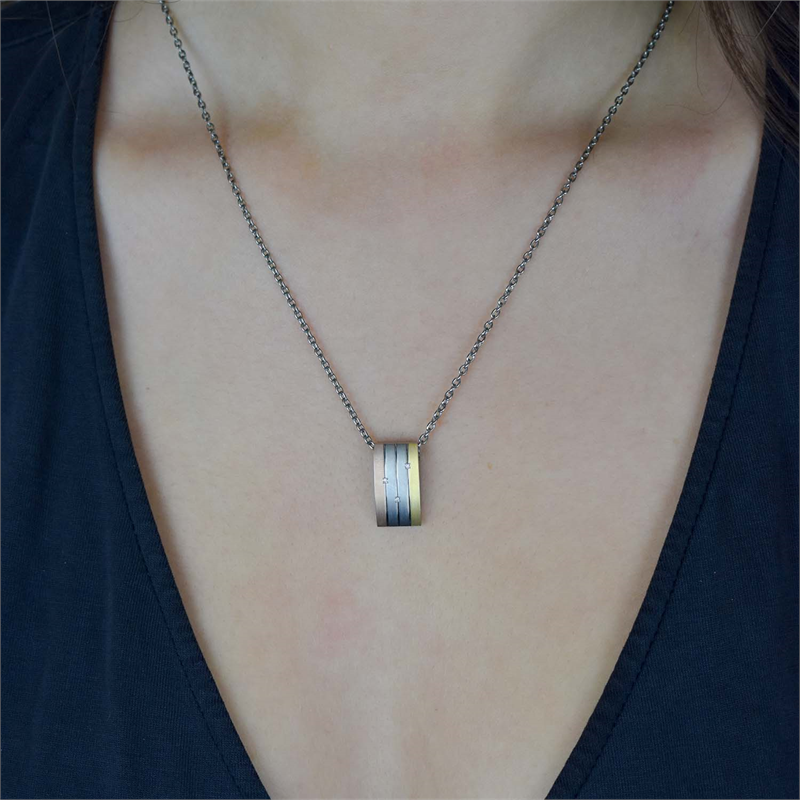 Een persoon draagt de Boccia Titanium Hanger Tricolor dia 3/0.015 halsketting (0792-02) aan een fijne ketting, afgebeeld tegen een blote huid en een donker topje met V-hals.