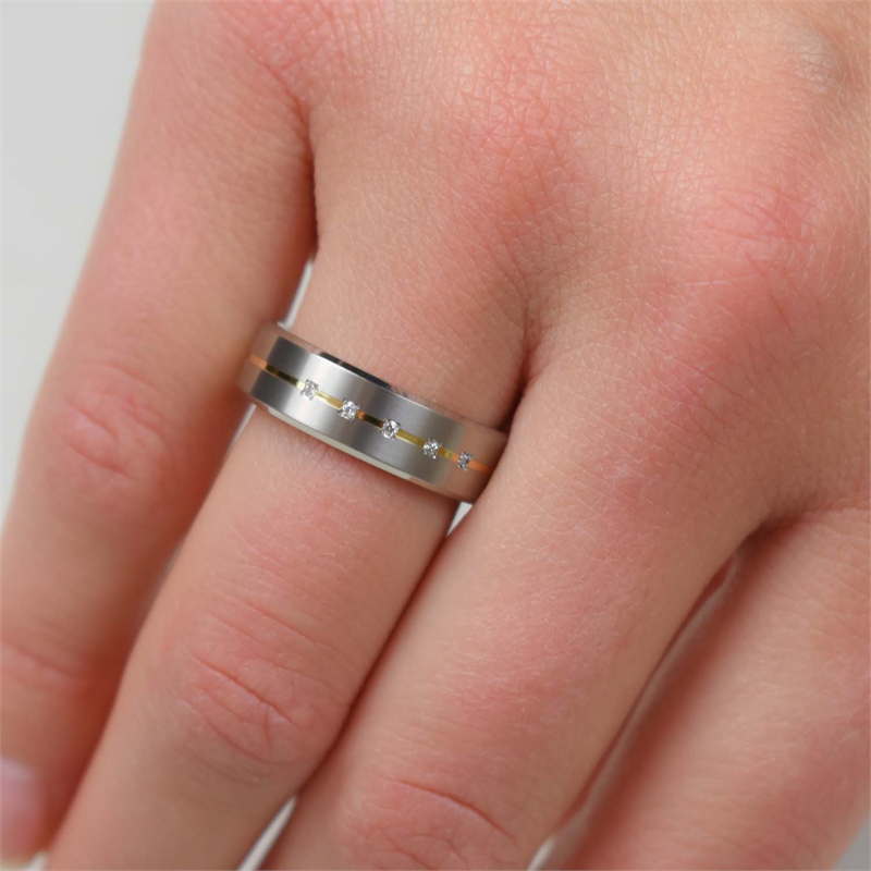 Een close-up van een hand met de Boccia Titanium Ring Bicolor dia 5/0.025 - 0101-19, een damesring van Boccia met ingelegde diamanten en een slank gouden accent, wat een elegant diamanten sieraad vormt.