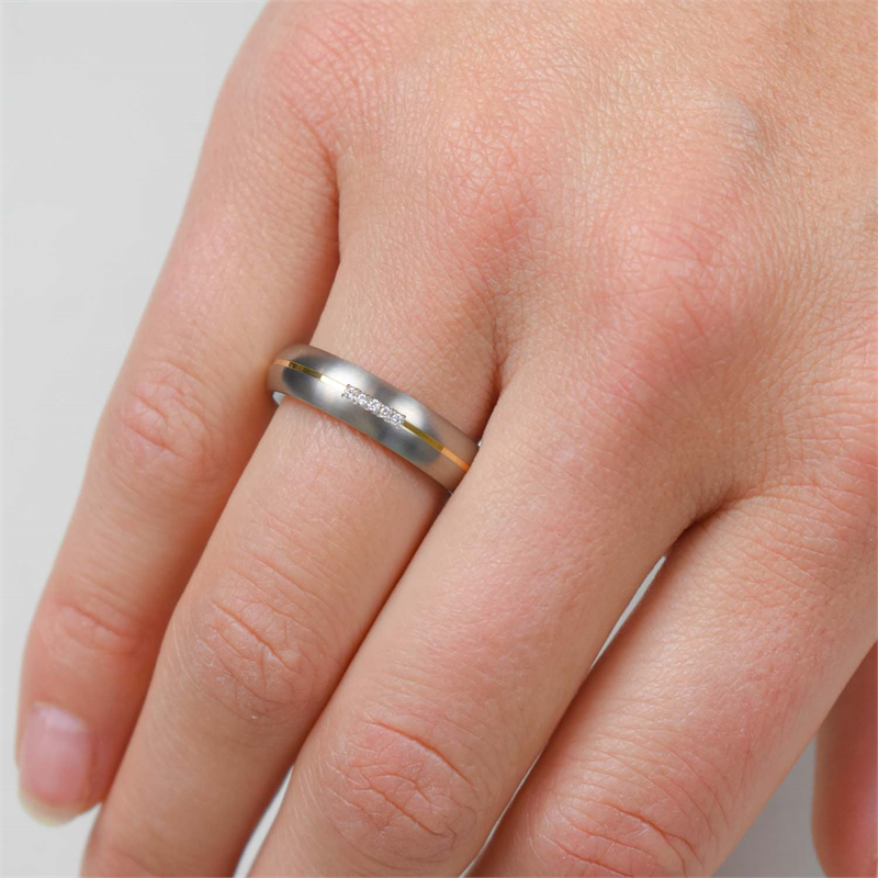 Een close-up toont een hand met de Boccia Titanium Ring Bicolor dia 5/0.025 - 0130-04 van Boccia. Deze ring heeft een gouden accentstreep en subtiele gravures op de ringvinger, aangevuld met korte, natuurlijke nagels.
