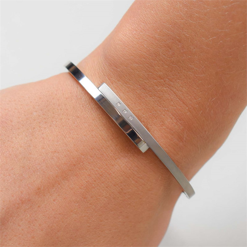 Een close-up van een pols versierd met de Boccia Titanium Armband Spang dia 3/0.015 - 03041-02, met een slanke rechthoekige staaf en subtiele gravures. De effen, lichte achtergrond benadrukt deze elegante Boccia dames sieraad.