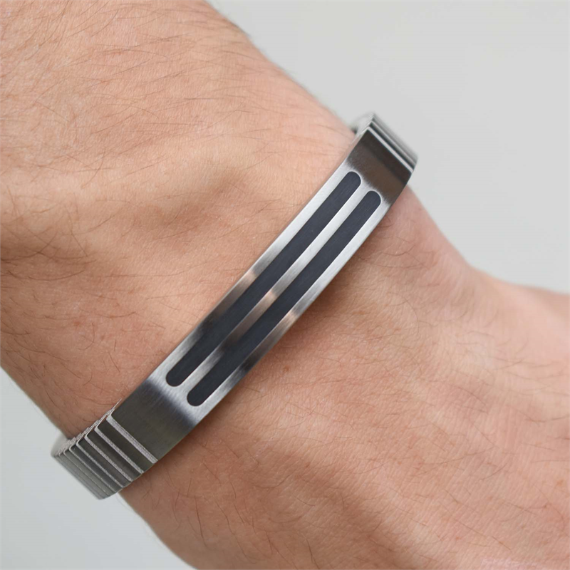 Een close-up van een pols met de Boccia Titanium Armband Spang emaille 0340-02 van Boccia. Deze armband heeft een strak design met twee parallelle zwarte emaille accenten en geribbelde randen.