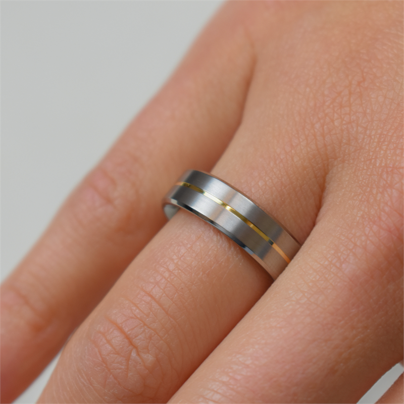 Een Boccia Titanium Ring Bicolor 0101-21, met een zilveren band met een dun gouden streepje, siert de ringvinger van een lichte hand tegen een eenvoudige achtergrond: een elegante damesring van Boccia.