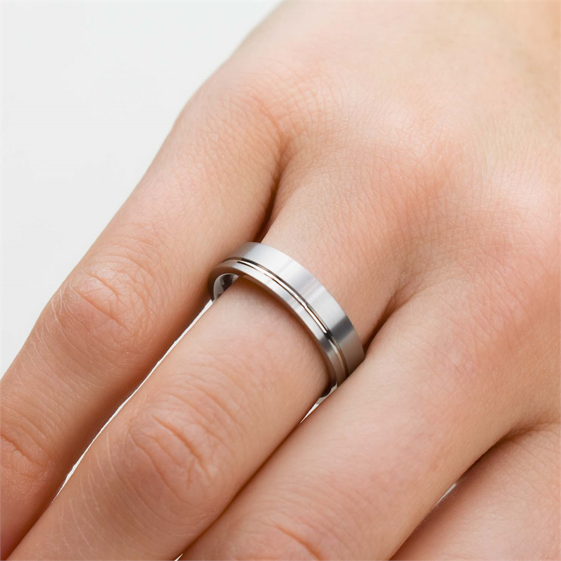 Een hand met een lichte huid draagt de Boccia Titanium Ring 0149-01 aan de ringvinger. De strakke metalen ring van Boccia heeft een eenvoudig, modern design met een glanzende afwerking tegen een effen witte achtergrond.