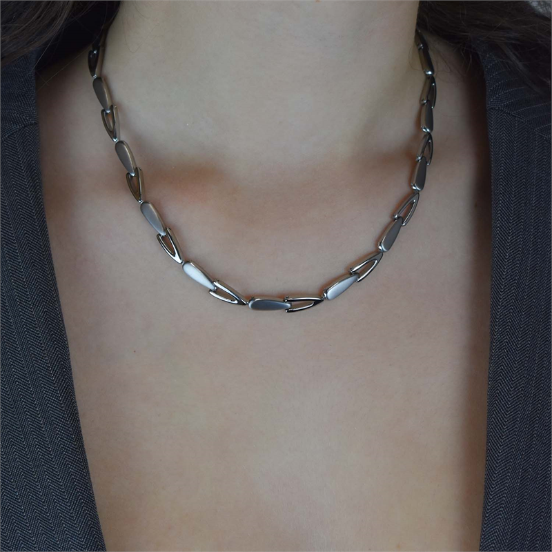 Een close-up van een persoon die de Boccia Titanium Collier 08039-01 draagt, met langwerpige ovale schakels. De strakke ketting contrasteert mooi met een donker V-hals colbert en accentueert de hals en de bovenkant van de borst voor een moderne look.