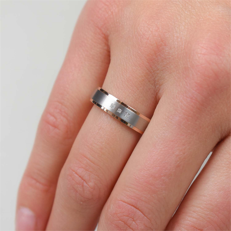 Een close-up van een blanke hand die de Boccia Titanium Ring Bicolor rgp dia 3/0.015 - 0134-02 van Boccia om de middelvinger draagt. De ring heeft een gladde, gepolijste afwerking met gegraveerde details.