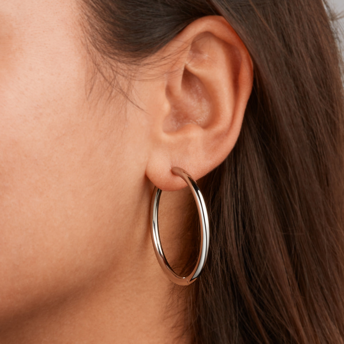 Close-up van het oor van een vrouw die Boccia Titanium Oorringen 05070-01 draagt, haar steile bruine haar is gedeeltelijk zichtbaar. Deze elegante gouden oorbellen van Boccia voegen een stralende toets toe aan elke sieradencollectie.