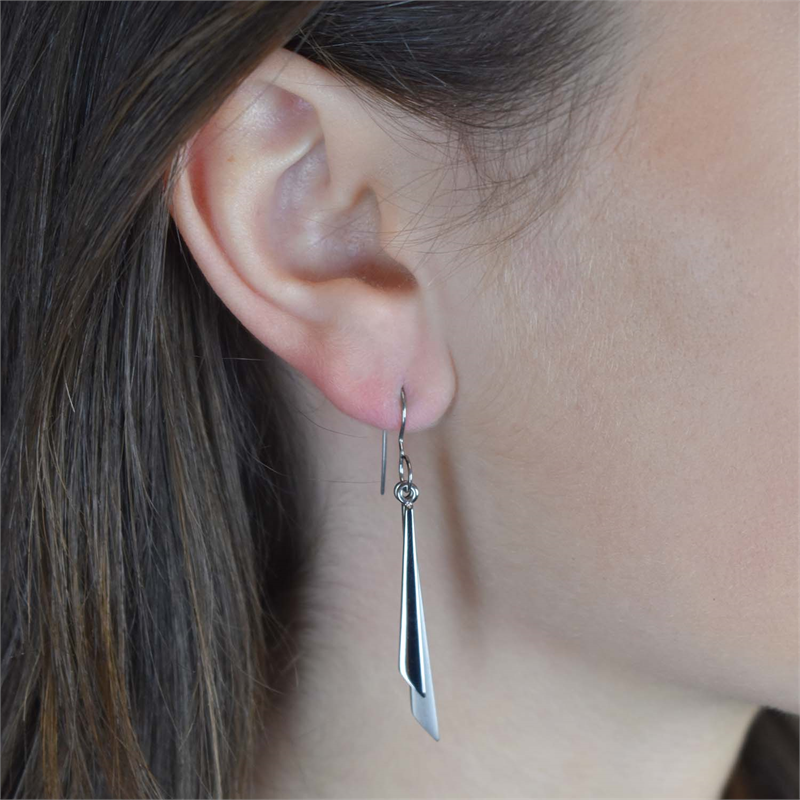 Close-up van het oor van een persoon die Boccia Titanium Oorhangers 0565-01 draagt: lange, glanzende, geometrische oorbellen van Boccia, gemaakt van duurzaam titanium. De oorbellen hangen aan de oorlel, waarbij het bruine haar gedeeltelijk zichtbaar is naast het oor.