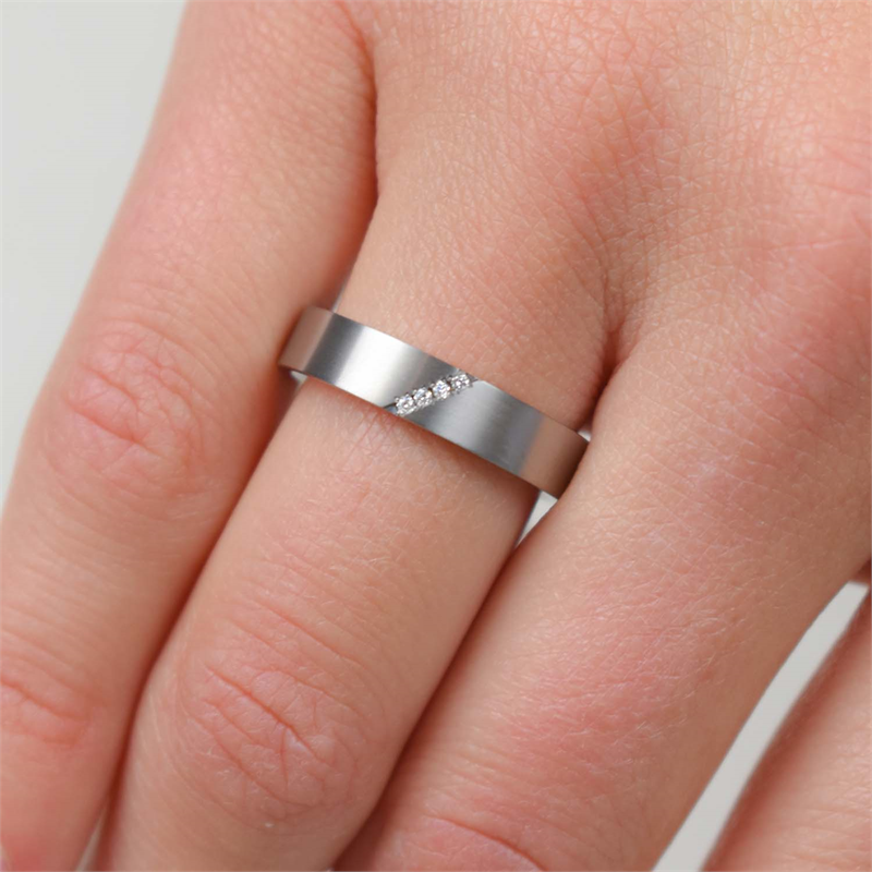 Een eerlijke hand toont de Boccia Titanium Ring dia 4/0.02 - 0121-07, een matzilveren band van Boccia met een diagonale rij fonkelende diamanten, elegant gedragen om de middelvinger.