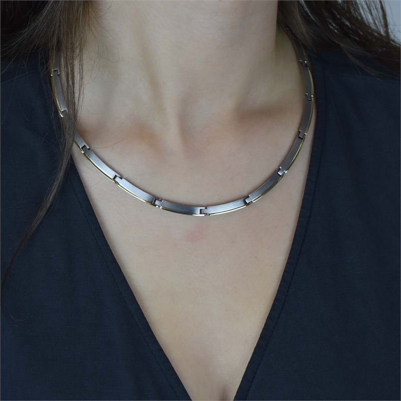 Een close-up van iemand die de Boccia Titanium Collier Bicolor 08028-02 met rechthoekige schakels en een minimalistisch design draagt, gecombineerd met een donkere top met V-hals. Het gezicht van de persoon is niet zichtbaar. Merk: Boccia.
