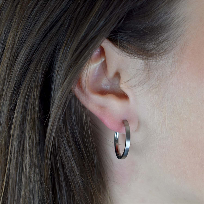 Een close-up van iemands oor met sluik bruin haar, gekleed in Boccia Titanium Oorringen 0517-01 - elegante, zilverkleurige oorbellen van Boccia die schitteren met hun duurzame titanium ontwerp.