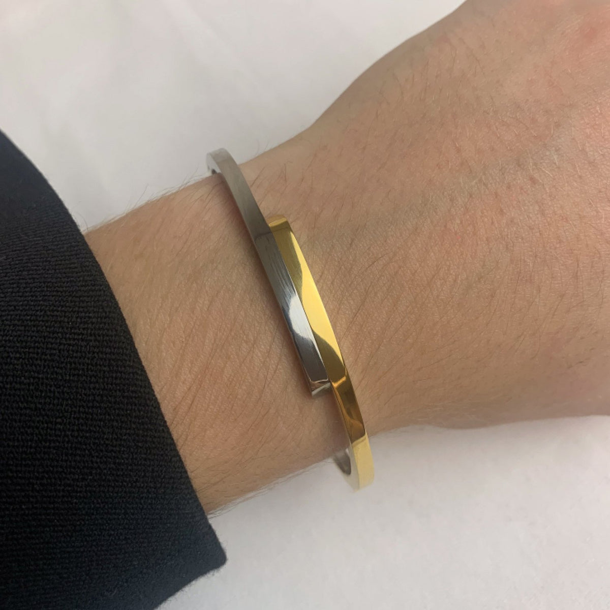Een close-up toont een pols met de Boccia Titanium Armband Spang Bicolor NL 03041-05, met elegante gouden en zilveren tinten van Boccia, gedragen over een zwarte hoes.