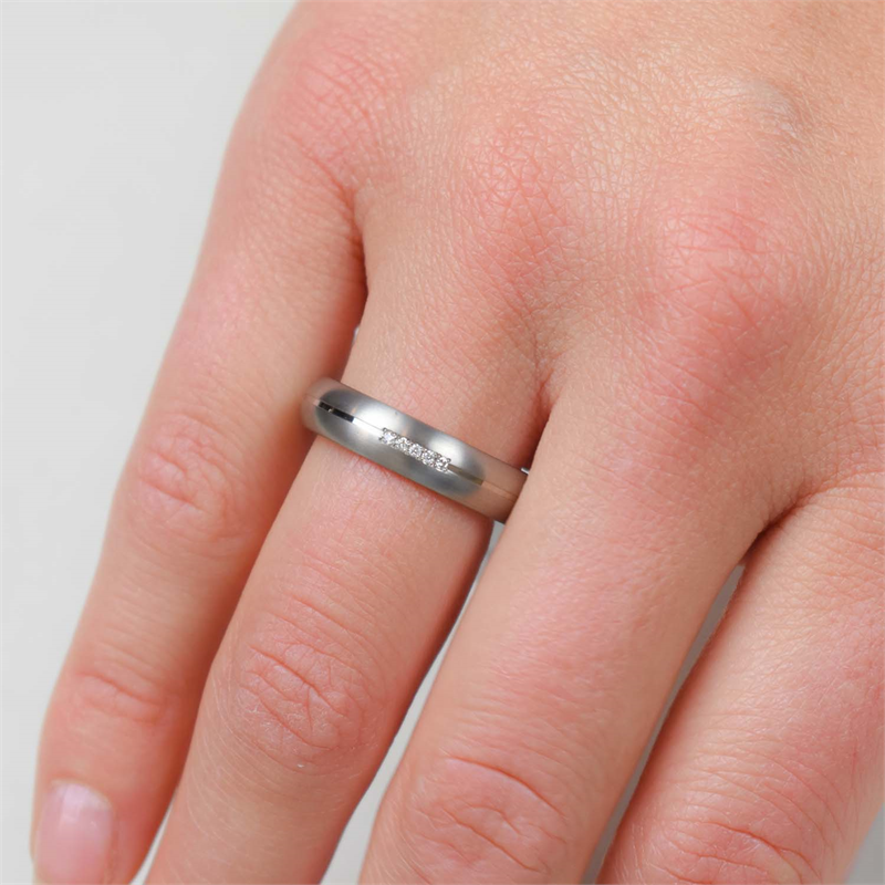Een close-up van een hand met de Boccia Titanium Ring dia 5/0.025 - 0130-03 van Boccia, met kleine ingelegde diamanten op de ringvinger tegen een lichte, neutrale achtergrond.