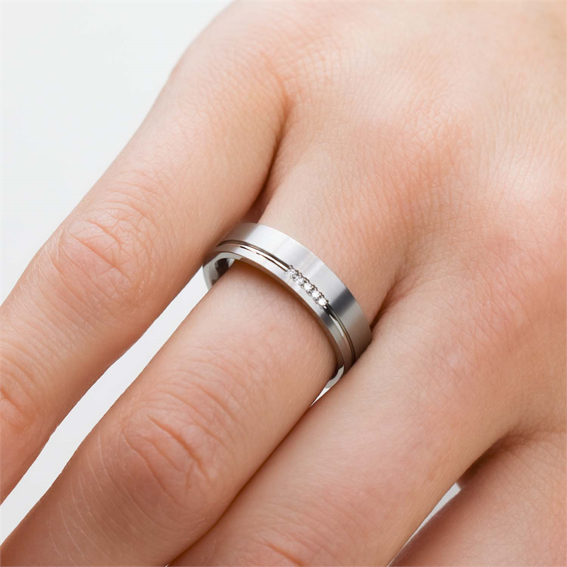 Een close-up van een hand versierd met de elegante Boccia Titanium Ring dia 5/0.025 - 0149-02 op de ringvinger, waarbij de gepolijste titanium afwerking en de rij ingelegde diamanten tegen een neutrale achtergrond goed tot hun recht komen.