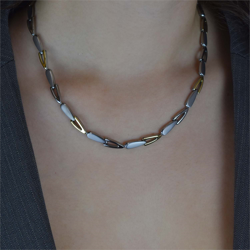 Een persoon die de Boccia Titanium Collier Bicolor 08039-02 draagt, met langwerpige zilver- en goudkleurige schakels, in combinatie met een donkere blazer met textuur.