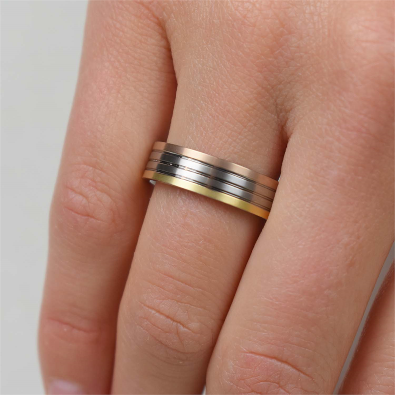 Een close-up toont een hand met de Boccia Titanium Ring Tricolor 0135-03 van Boccia, met parallelle banden van goud, zilver en zwart titanium op de middelvinger tegen een effen, lichte achtergrond.