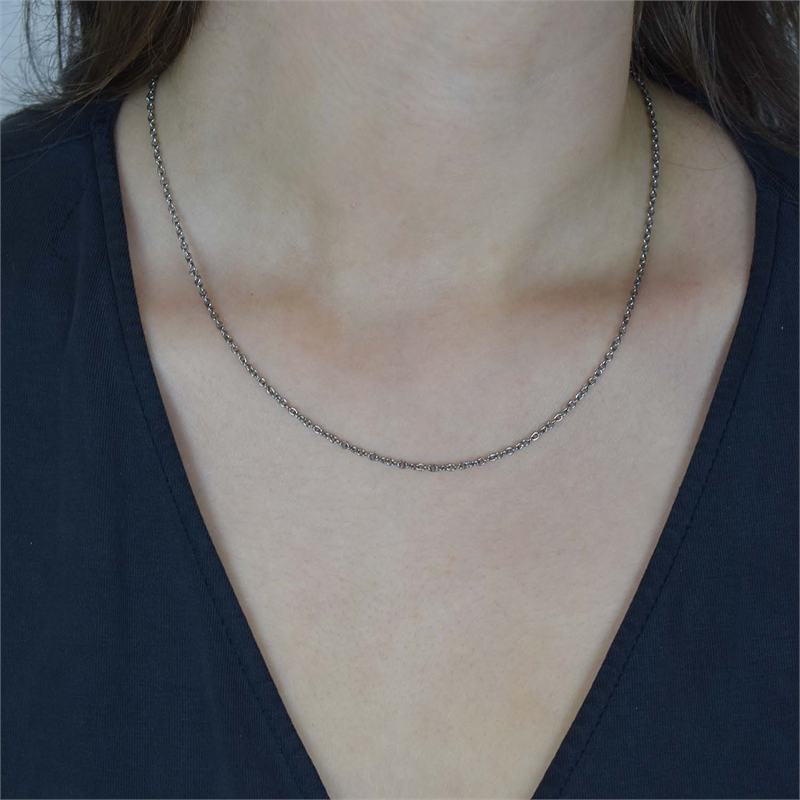 Een close-up toont een persoon die de Boccia Titanium Lengte Collier 0819-01 draagt, een dunne, zilverkleurige halsketting van Boccia met een eenvoudig ontwerp, gecombineerd met een donkere top met V-hals tegen een effen achtergrond.