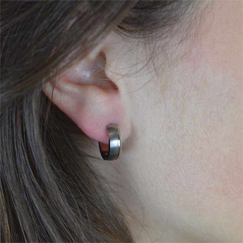 Close-up van een persoon met een lichte huidskleur en bruin haar die Boccia Titanium Oorringen 0539-11 draagt; de kleine metalen oorbellen worden gedeeltelijk bedekt door hun haar.