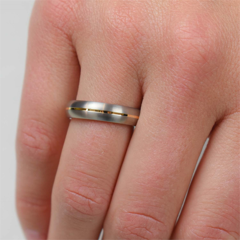 Een close-up van een hand met de Boccia Titanium Ring Bicolor 0130-02, met een dunne gouden streep in het midden, afgebeeld op de ringvinger tegen een lichte achtergrond - ideaal om te bewaren in je sieradendoosje.