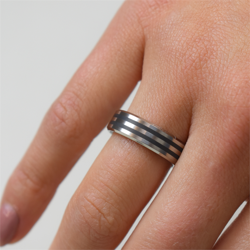 Een hand versierd met een Boccia Titanium Ring zwart emaille 0101-17, met zwarte en zilveren horizontale strepen, siert de effen achtergrond.