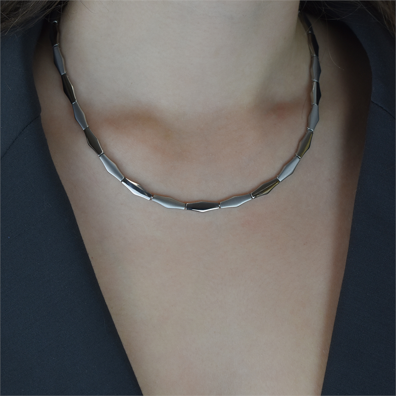 Een persoon in een zwarte blazer draagt een Boccia Titanium Collier NL 08047-01, die het geometrische, rechthoekige ontwerp laat zien. De close-up benadrukt de halslijn en de opstelling van de ketting.