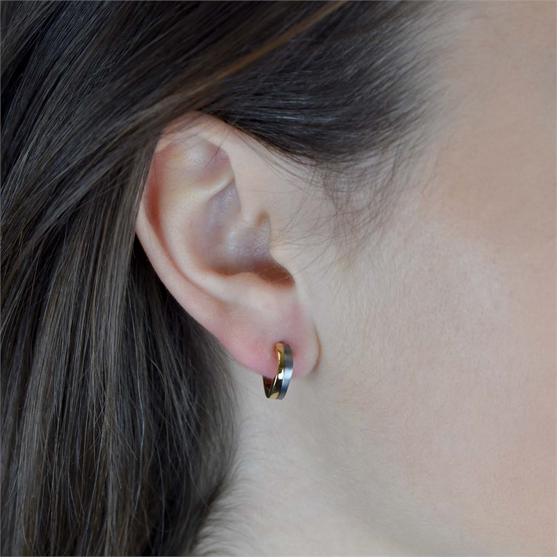 Close-up van een persoon die een Boccia Titanium Oorring Bicolor 0563-02 draagt, met een glanzend goudkleurig accent. Het bruine haar is achter het oor gestopt, waardoor een gladde, lichte huid wordt benadrukt. Van Boccia, gemaakt voor dagelijkse elegantie.