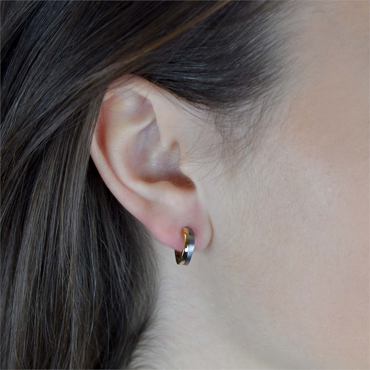 Close-up van een persoon die een Boccia Titanium Oorring Bicolor 0563-02 draagt, met een glanzend goudkleurig accent. Het bruine haar is achter het oor gestopt, waardoor een gladde, lichte huid wordt benadrukt. Van Boccia, gemaakt voor dagelijkse elegantie.