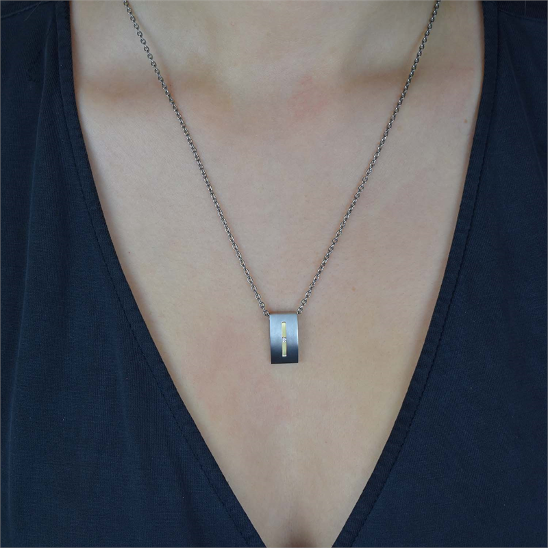 Een persoon draagt de Boccia Titanium Hanger Bicolor (0718-01) ketting, met een klein gouden kruis op de hanger. Gekleed in een zwarte top met v-hals, stralen ze subtiele elegantie uit.