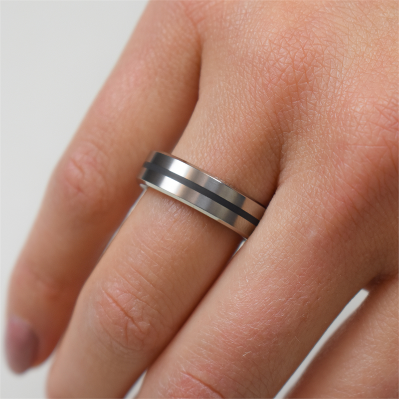Een hand toont de elegante Boccia Titanium Ring zwart emaille 0101-14, met twee zwarte strepen als zwart emaille. Deze strakke ring van Boccia siert de middelvinger tegen een lichte achtergrond.