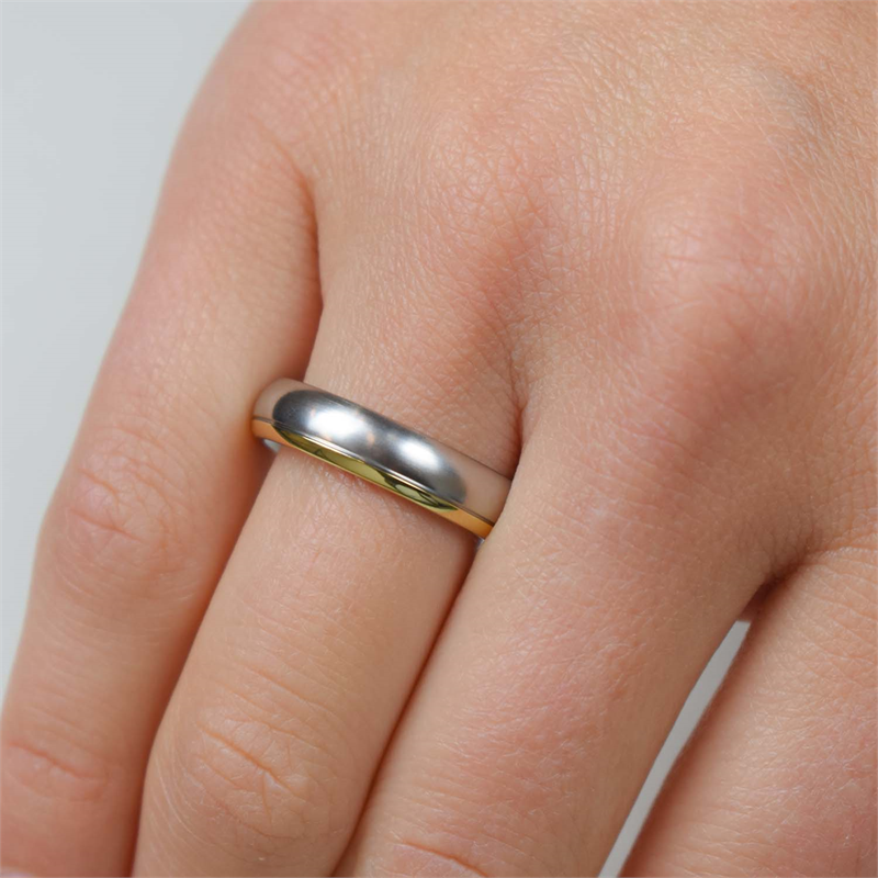 Een close-up van een hand die de Boccia Titanium Ring Bicolor 0130-08 van Boccia draagt. Het gladde, glanzende zilver- en goudkleurige titaniumontwerp met een gouden accent op de ringvinger tegen een lichte achtergrond.