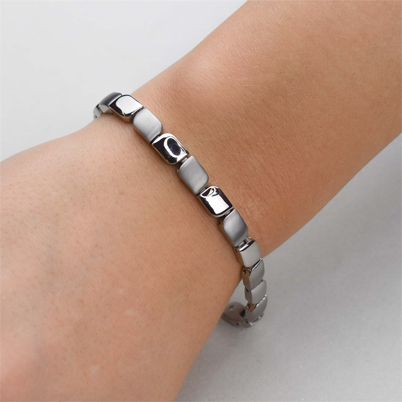Een close-up van de pols van een persoon die de Boccia Titanium Armband 03007-01 draagt, met een zilverkleurig, modern rechthoekig schakelontwerp, tegen een effen lichtgekleurde achtergrond.