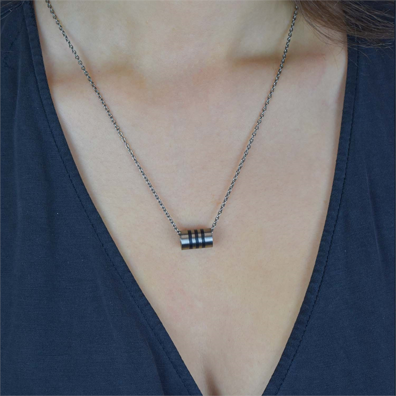 Een persoon draagt een donker V-hals shirt en een ketting met de Boccia Titanium Hanger 0719-03, met drie zwarte strepen in zwart emaille. De cilindrische hanger van Boccia hangt midden op de borst.