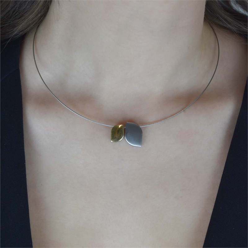 Een close-up toont een vrouw die de Boccia Titanium Hanger Bicolor 07009-01 ketting van Boccia draagt: een delicate, dunne ketting met twee gebogen bladhangers in goud en zilver. Gemaakt van duurzaam materiaal, combineert ze de ketting met een donkere top met V-hals.