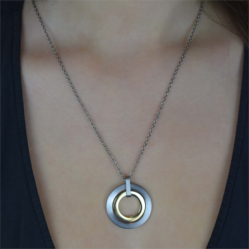 Een close-up toont een persoon die de Boccia Titanium Hanger Bicolor 0741-02 halsketting van Boccia draagt, met twee in elkaar grijpende zilveren en gouden ronde hangers aan een dunne ketting, rustend boven een donker V-hals topje.