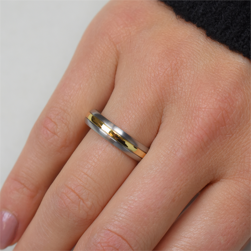 Een close-up van een hand die de Boccia Titanium Ring Bicolor 0131-02 van Boccia draagt, een gouden en zilveren titanium ring met een subtiel gouden accent op de ringvinger, natuurlijke nagels en zwarte stof zichtbaar bij de pols.