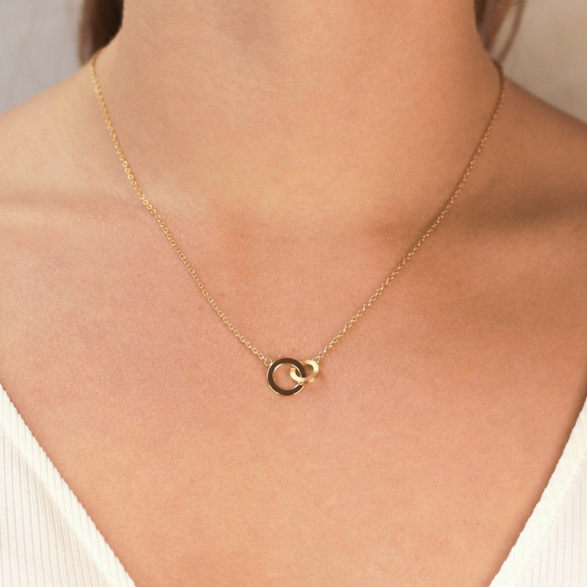 Een close-up van een vrouw die de Boccia Titanium Collier gp 08033-03, met twee in elkaar grijpende cirkels, tegen haar blote nek en sleutelbeen draagt. Ze is gekleed in een witte top met V-hals en textuur.