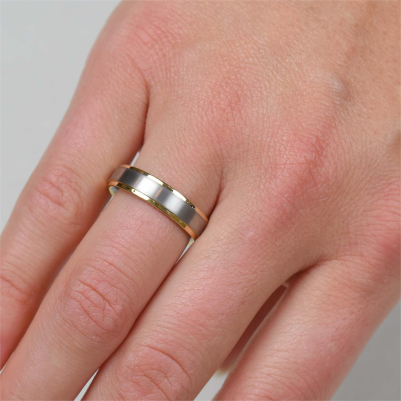 Een close-up van een hand met de Boccia Titanium Ring Bicolor 0134-05 van Boccia, waarbij de tweekleurige gouden en zilveren band op een lichtgrijze achtergrond zichtbaar is.