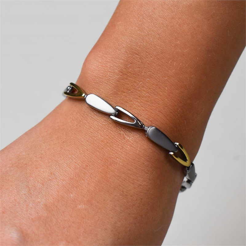 Een close-up toont een Boccia Titanium Armband op lichtbruine huid, met afwisselend zilveren en gouden langwerpige titanium schakels. De effen neutrale achtergrond accentueert deze elegante damesarmband van Boccia.