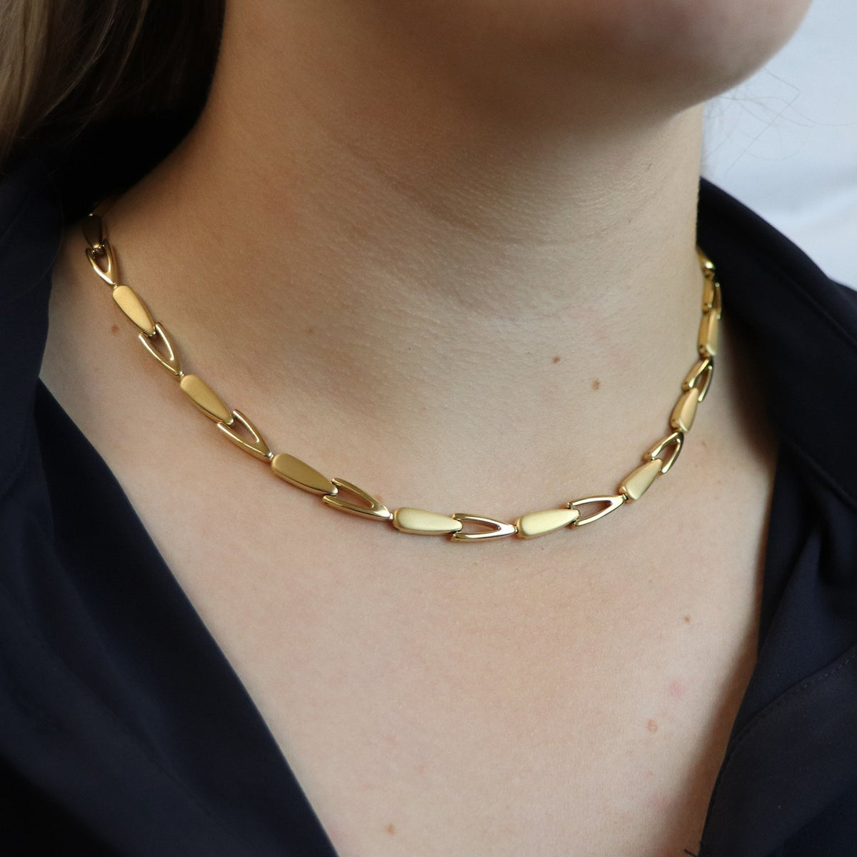 Een close-up van een persoon die de Boccia Titanium Collier gp 08039-03 draagt, een goudkleurige ketting met grote platte schakels van Boccia, gecombineerd met een donkere top. Alleen de hals en kraag zijn zichtbaar, wat deze stijlvolle sieraden extra benadrukt.