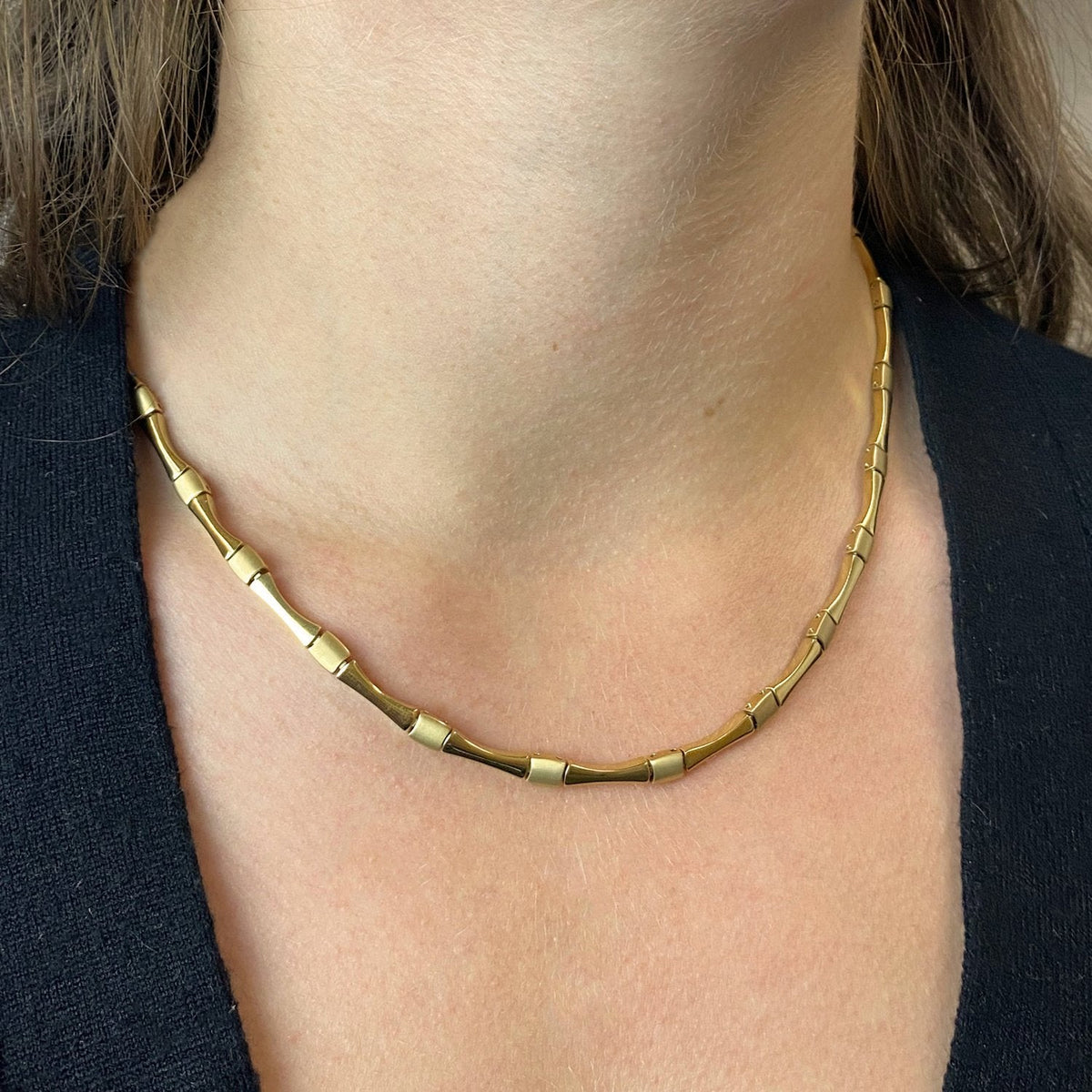 Een persoon draagt de Boccia Titanium Collier gp 08045-03, een stevige goudkleurige geometrische schakelketting van Boccia, met klapsluiting, gestyled tegen de blote huid en een zwarte top.